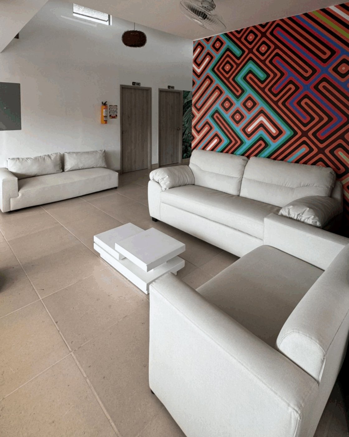 Sala de estar con sofás blancos, mesas bajas y mural geométrico