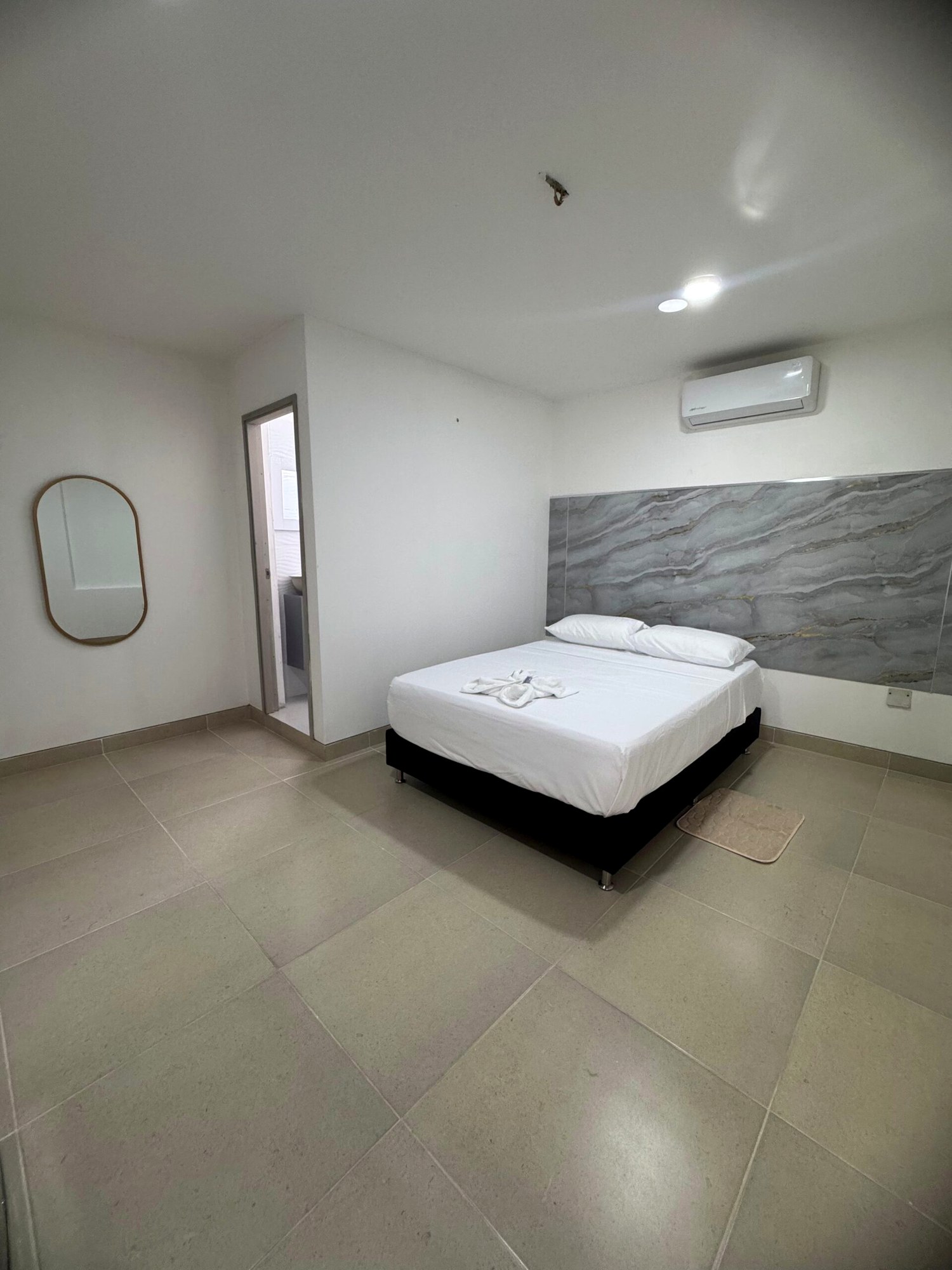 Habitación con cama doble, ropa de cama blanca, aire acondicionado y cabecero gris