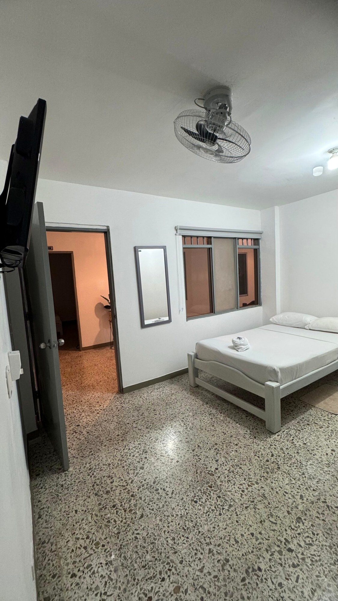 Habitación estándar con una cama, ropa de cama blanca, televisor y ventilador de techo